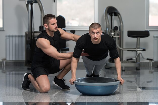 Persönlicher Trainer hilft Mann bei Bosu-Liegestützen