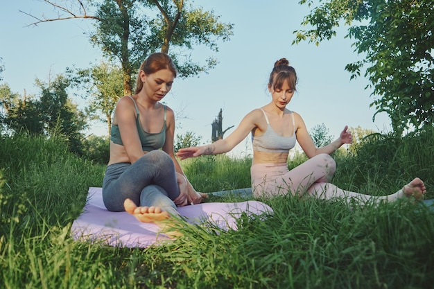 Persönlicher Yoga-Trainer, der junge Frau oder ihre Freundin Gomukhasana im Freien unterrichtet