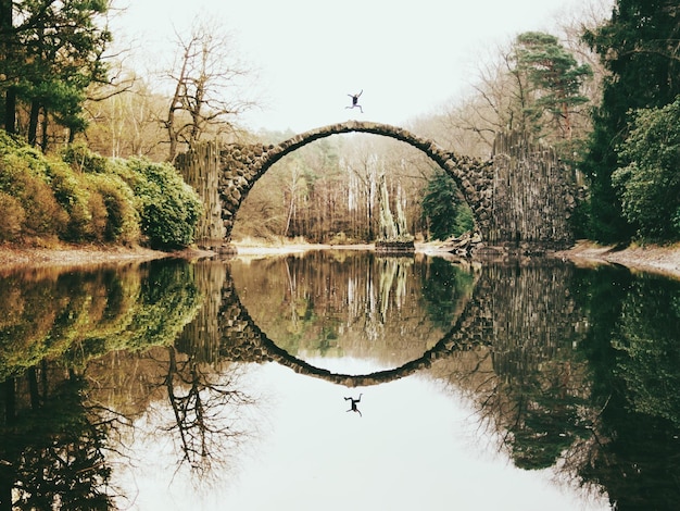 Foto person, die auf der rakotzbrucke-brücke über den fluss springt