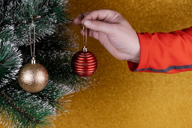 Person, die dekorationen auf einen weihnachtsbaum mit goldenen und roten kugeln setzt