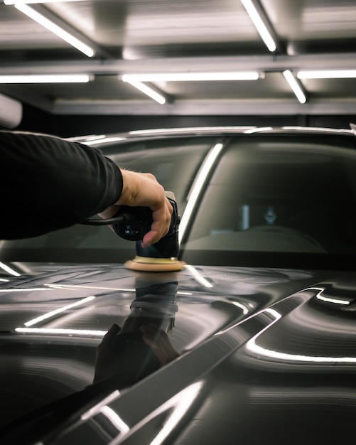 Person, die die Motorhaube eines modernen schwarzen Autos unter den Lichtern poliert