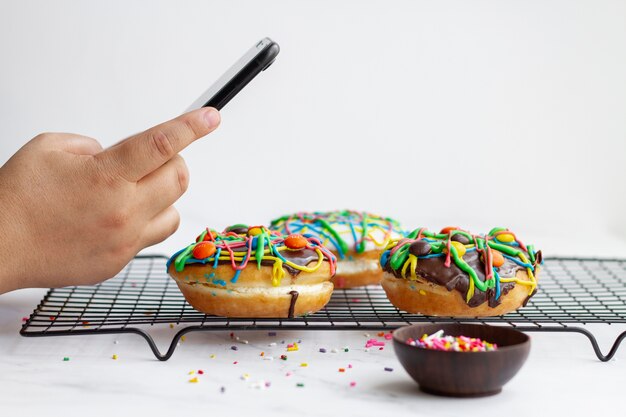 Foto person, die donuts mit buntem belag mit smartphone fotografiert