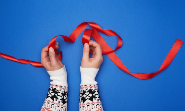 Person, die ein rotes Satinband auf einer blauen Oberfläche hält