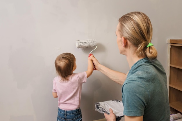 Person, die einen Farbrollen über einer grauen Wand hält, Vater mit Kind, der Dekoration und Neugestaltung des Raumes macht