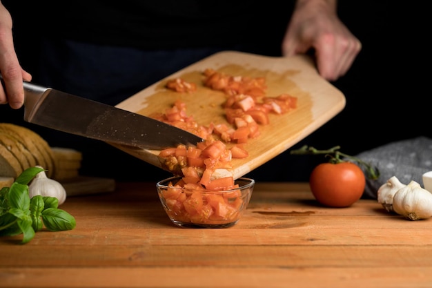 Person, die italienische Bruschette-Tomatenwürfel auf dunklem Hintergrund des Holzbretts zubereitet