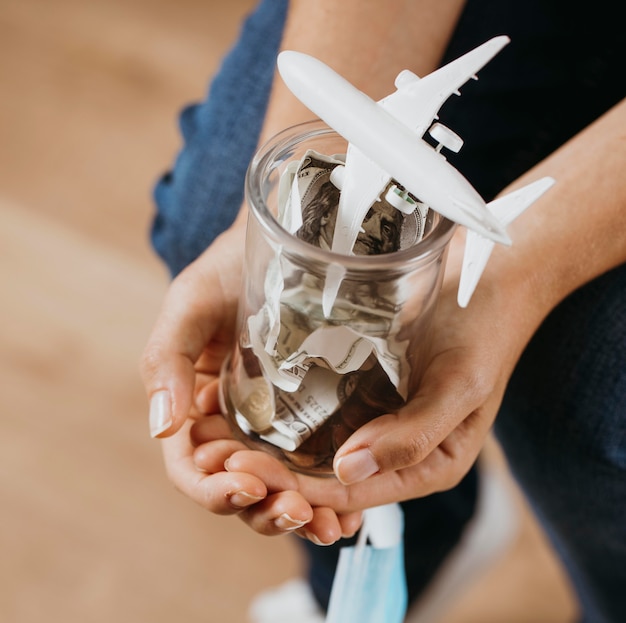 Foto person, die klares glas mit geld und flugzeugfigur hält