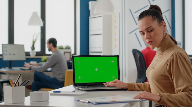 Person, die mit grünem Bildschirm auf Laptop im Geschäftsbüro arbeitet. Mitarbeiterin, die Computer mit isoliertem Mock-up-Hintergrund und Chroma-Key-Vorlage auf dem Display verwendet. Leerer Bildschirm für den Kopierbereich