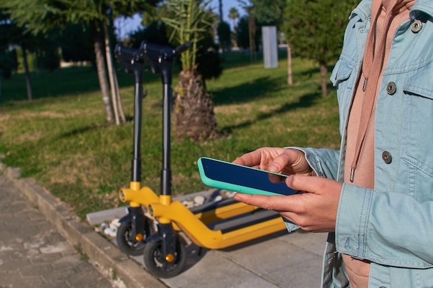 Person, die Smartphone und mobile App verwendet, um einen Roller für schnelles mobiles aktives Fahren durch die Stadt zu mieten