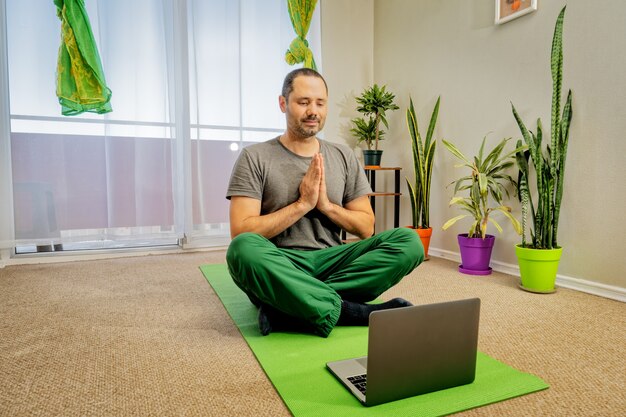 Person, die zu Hause auf dem Boden sitzt und Yoga mit Laptop macht