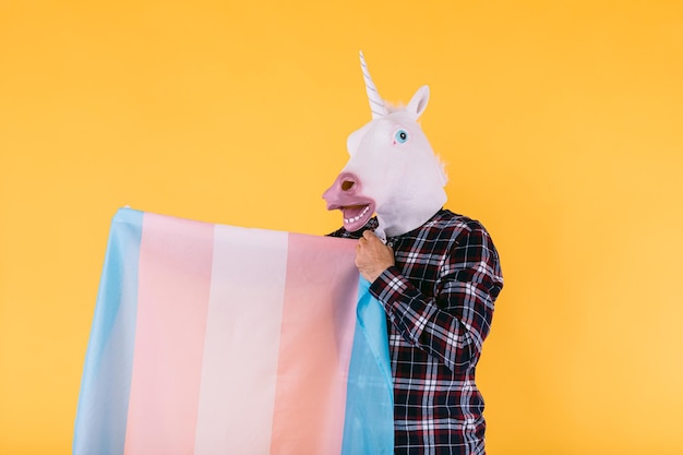 Person, gekleidet in Einhornmaske mit kariertem Hemd, das Transgender-Flagge auf gelbem Hintergrund hält Konzept der schwulen Pride Transsexualität Geschlecht binäre Lesben- und lgtbq-Rechte