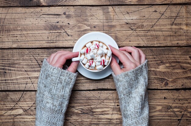 Person hält eine Tasse heiße Schokolade mit Marshmallows und Zuckerstange