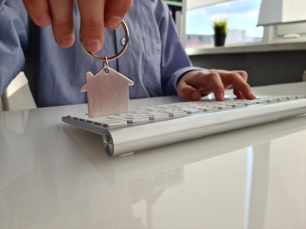 Person hält Hausschlüssel und Schlüsselbund in Form von Haus auf der Laptoptastatur