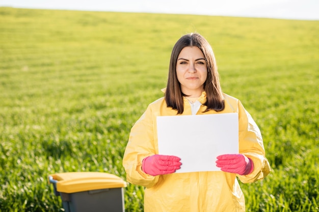 Person im Overall hält Papier mit leerem Blatt Papier für die Textbeschriftung, während sie auf der grünen Wiese steht Konzept der schlechten Ökologie und des Umweltschutzes