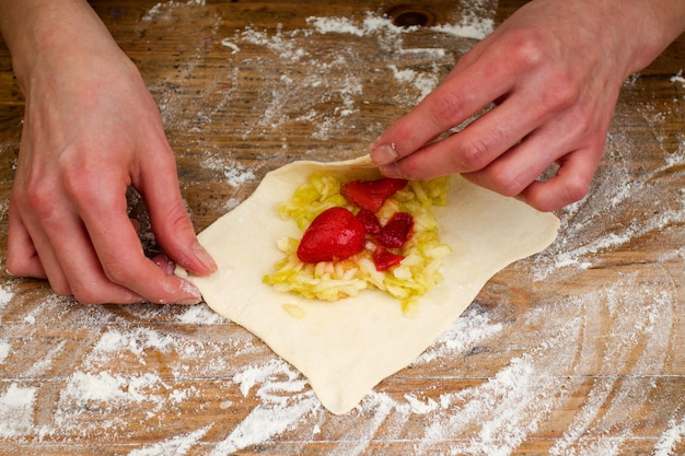 Person macht Gebäck mit Erdbeeren und Apfel