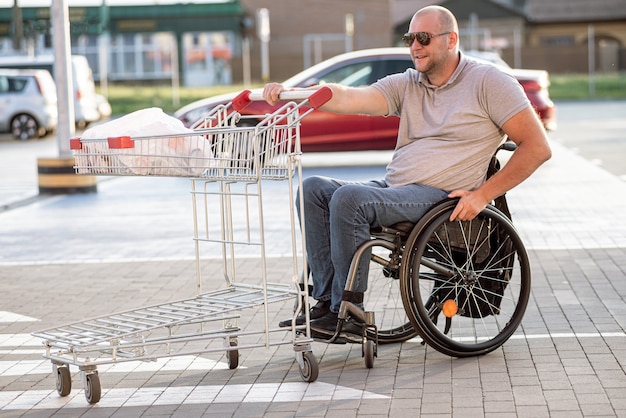 Person mit einer körperlichen behinderung, die auf einem supermarktparkplatz einen einkaufswagen vor sich her schiebt