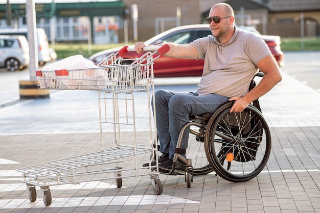 Person mit einer körperlichen Behinderung, die auf einem Supermarktparkplatz einen Einkaufswagen vor sich her schiebt