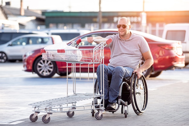 Person mit einer körperlichen Behinderung, die auf einem Supermarktparkplatz einen Einkaufswagen vor sich her schiebt