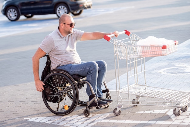 Person mit einer körperlichen Behinderung, die auf einem Supermarktparkplatz einen Einkaufswagen vor sich her schiebt