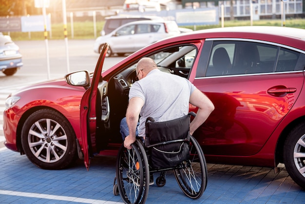 Person mit einer körperlichen Behinderung, die aus dem Rollstuhl in ein rotes Auto einsteigt