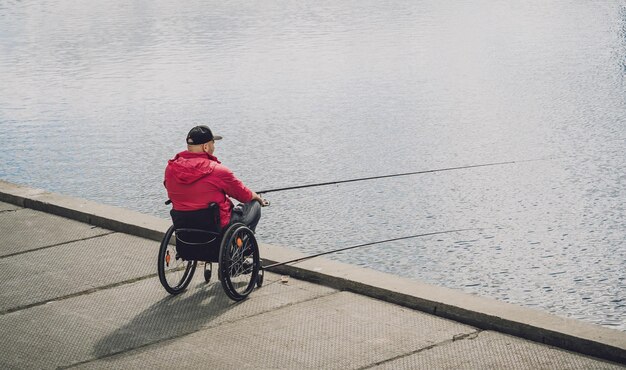 Person mit einer körperlichen Behinderung im Rollstuhl beim Angeln vom Angelpier