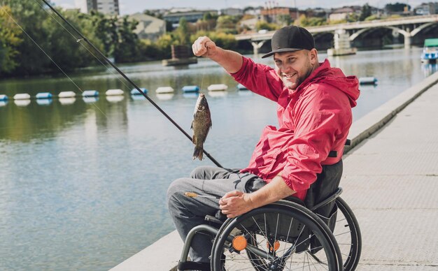 Person mit einer körperlichen Behinderung im Rollstuhl beim Angeln vom Angelpier