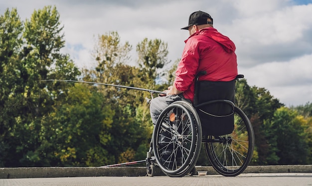 Person mit einer körperlichen Behinderung im Rollstuhl beim Angeln vom Angelsteg