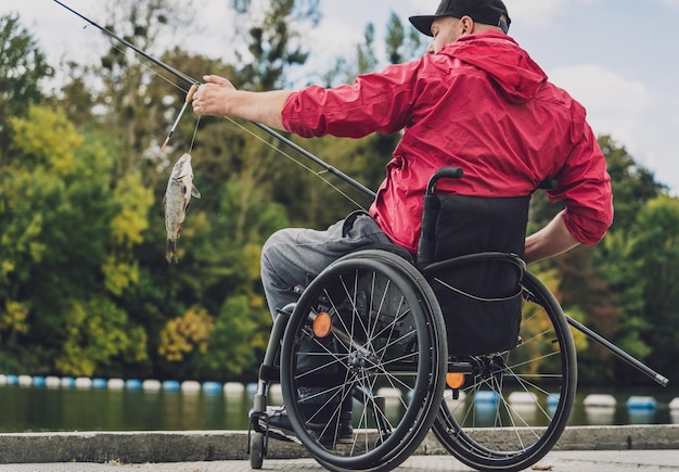 Person mit einer körperlichen Behinderung im Rollstuhl beim Angeln vom Angelsteg