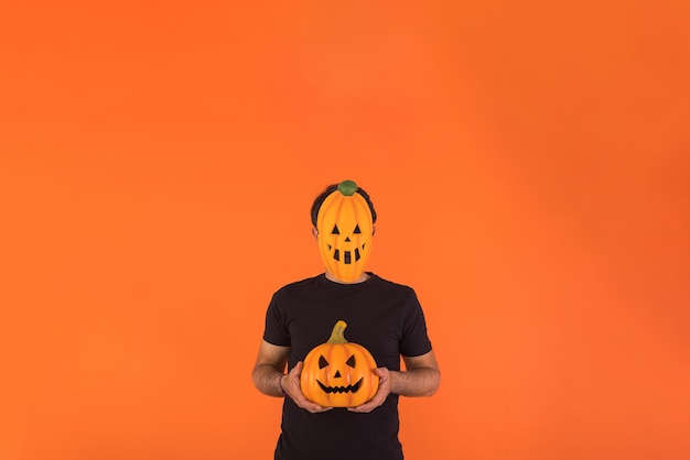 Person mit Kürbismaske, die Halloween feiert und einen Kürbis auf orangefarbenem Hintergrund hält Konzept der Feier Allerseelen und Allerheiligen