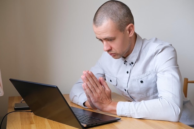 Person mit Laptop mit im Gebet gefalteten Händen.