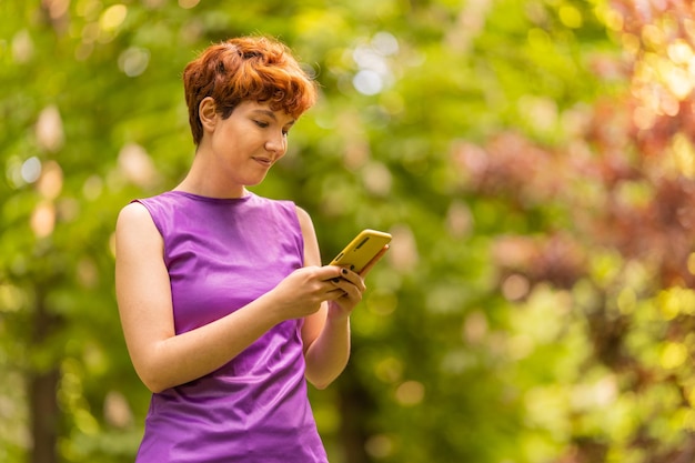 Person mit nichtbinärem Geschlecht, die ein Mobiltelefon im Park benutzt