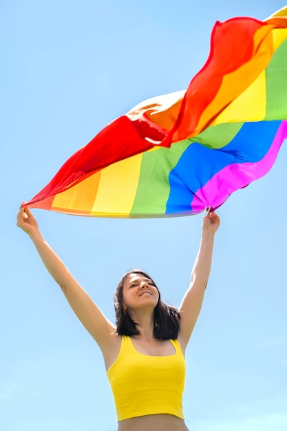 Person mit Regenbogen-LGBT-Flagge weht im Wind vor blauem Himmelshintergrund