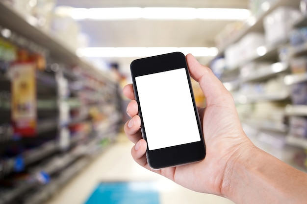 Person mit Smartphone weißen Bildschirmhalter auf der Hand mit Regalen auf Hintergrund im Supermarkt.