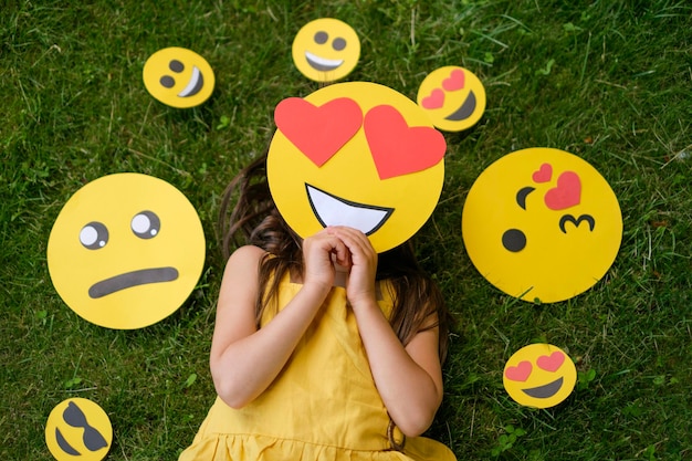 La persona está acostada sobre la hierba cubriendo la cara con un emoticono cariñoso