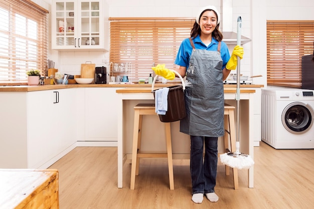 Una persona alegre está de pie en una cocina luminosa con suministros de limpieza listos para hacer las tareas