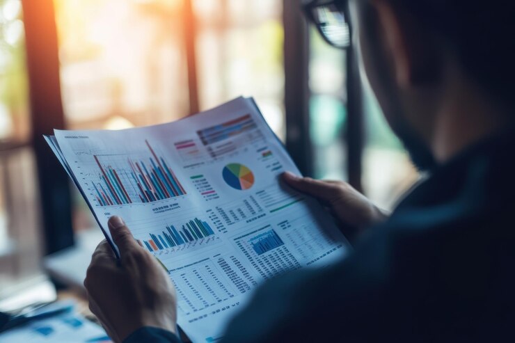 Una persona analiza datos financieros y gráficos tomando notas con un bolígrafo mientras sostiene un clipboard que refleja profesionalismo y diligencia