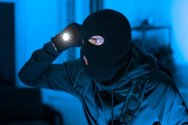 Persona con balaclava iluminando una linterna en una habitación oscura