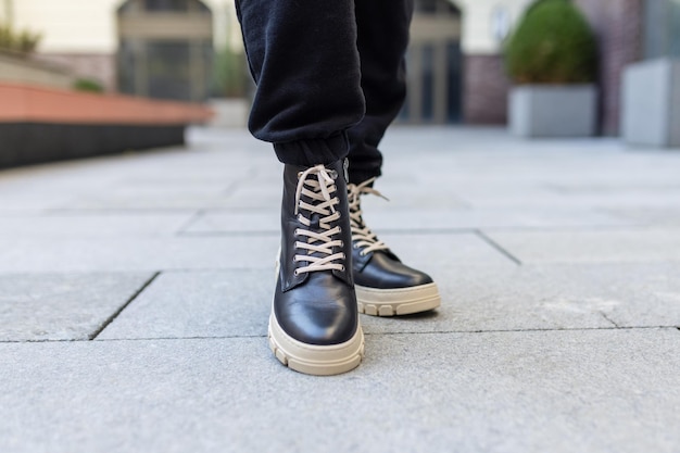 Una persona con botas de cuero negro con cordones blancos y un par de jeans negros.