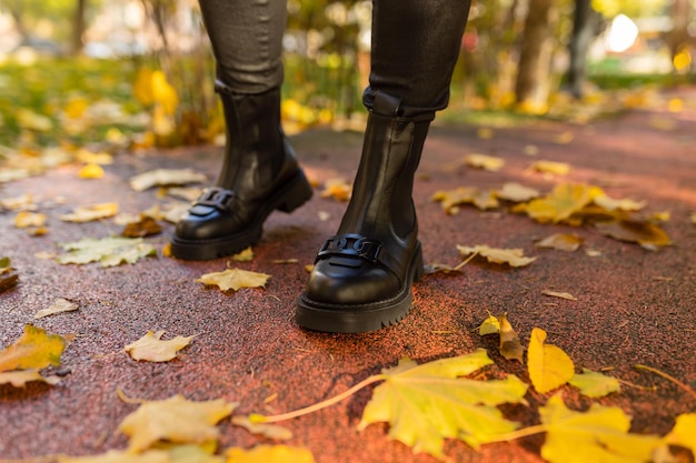 Una persona con botas negras se para en una acera mojada en hojas de otoño.