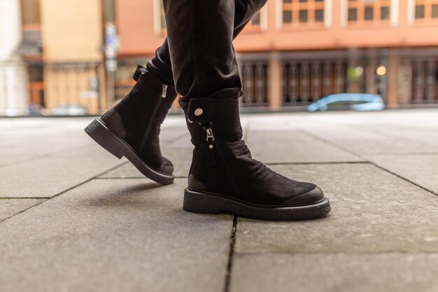 Una persona con botas negras con una hebilla plateada en el lateral.