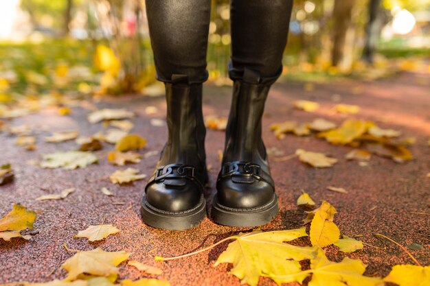 Una persona con botas negras se para en un suelo húmedo frente a las hojas de otoño.