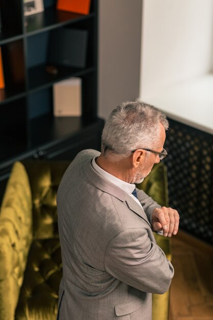 Persona canosa. Vista lateral de un hombre de pelo gris con un elegante traje mientras está de pie y mirando hacia abajo en su oficina