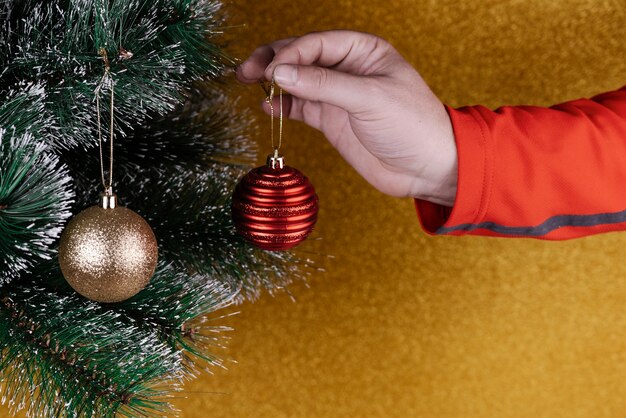 Persona colocando adornos en un árbol de Navidad con bolas rojas y doradas