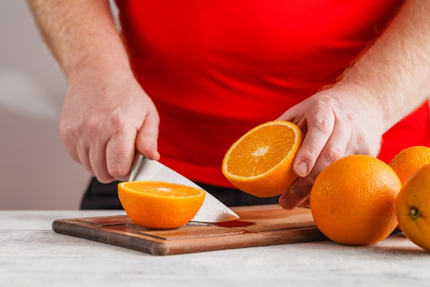 Persona cortando para hacer jugo de naranjas frescas en la mesa de madera