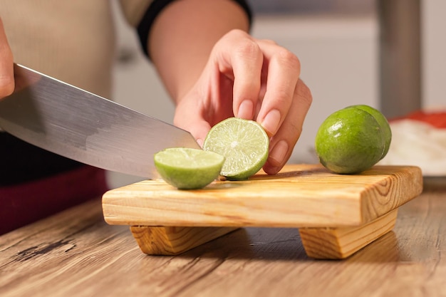 Persona cortando un limón verde con un cuchillo sobre una mesa de madera en su cocina