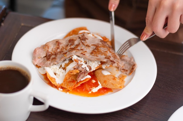 Persona desayunando tortillas con salsa roja en un plato blanco en el restaurante