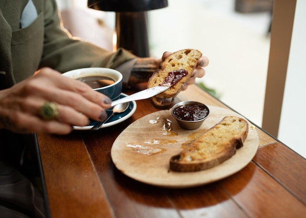 Persona desayunando tostadas y mermelada y bebiendo café en la cafetería