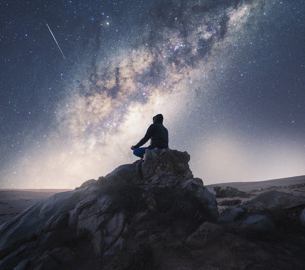 Persona desconocida meditando por la noche bajo la Vía Láctea en una colina