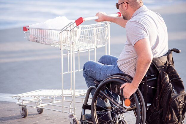 Persona con discapacidad física empujando el carro delante de sí mismo en el estacionamiento del supermercado