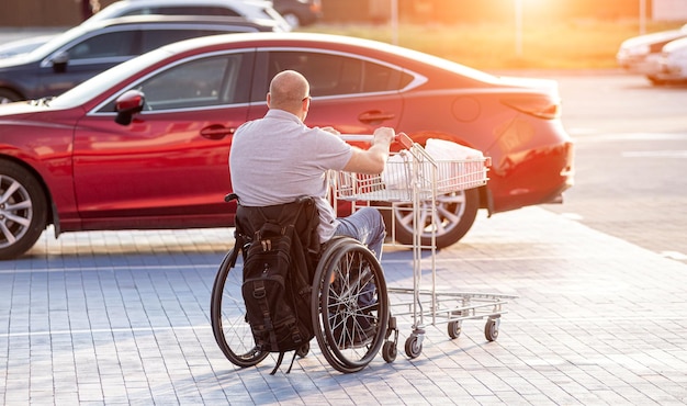 Persona con discapacidad física empujando el carro delante de sí mismo en el estacionamiento del supermercado