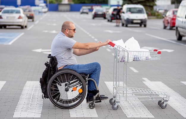 Persona con discapacidad física empujando el carro delante de sí mismo en el estacionamiento del supermercado